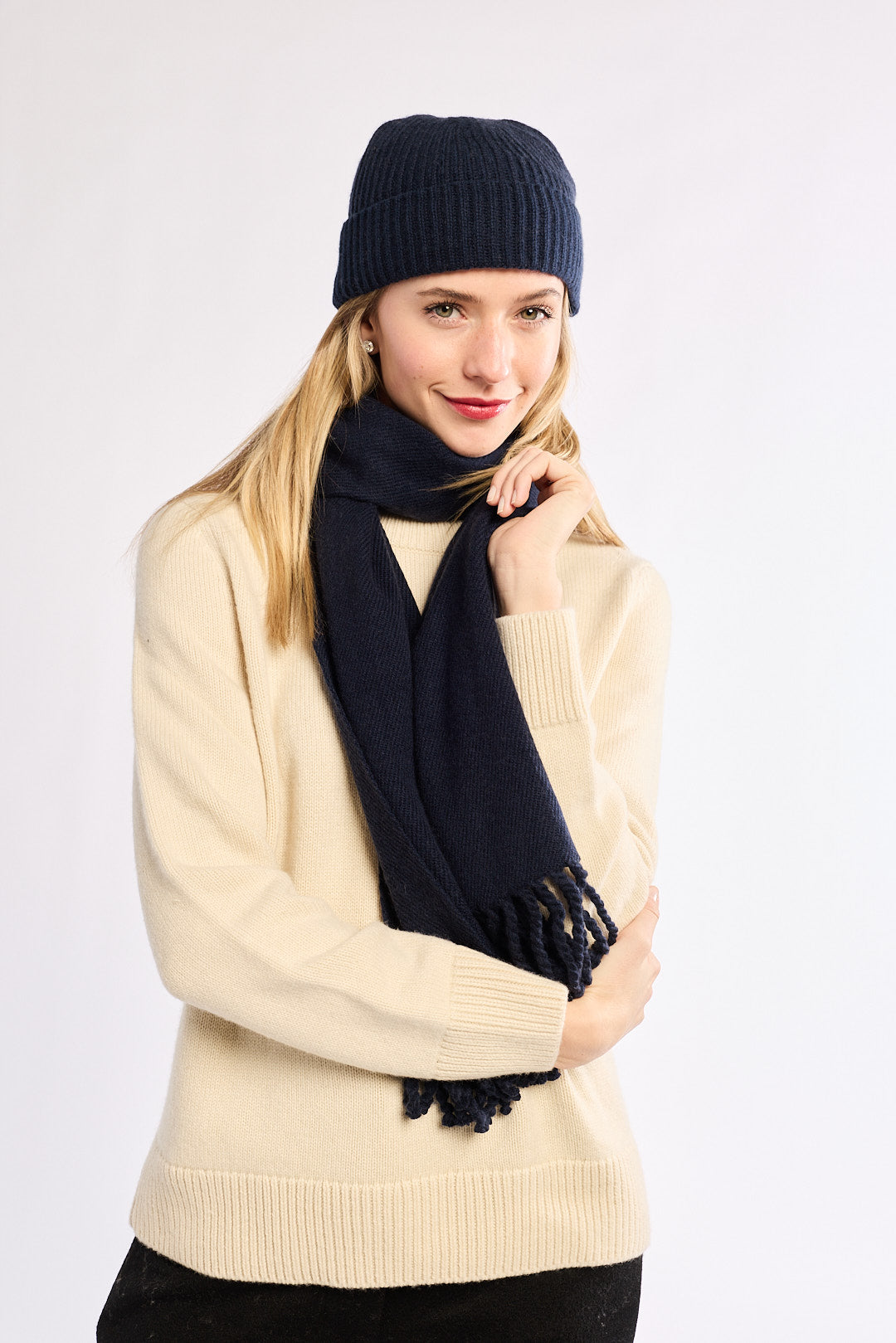 Woman wearing a navy beanie and scarf with a beige sweater on a white background