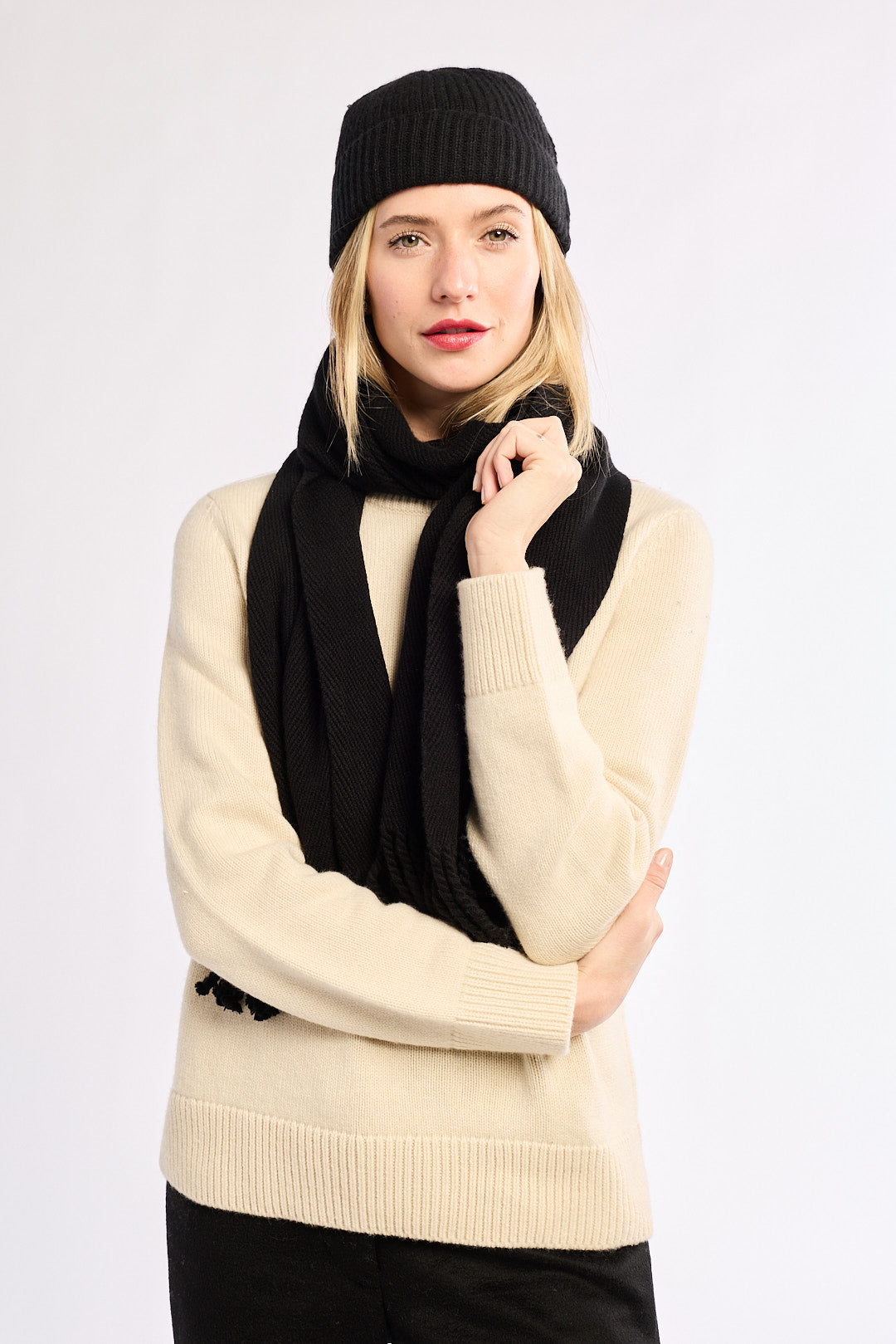 Woman wearing a black knit hat and scarf with a beige sweater on a white background