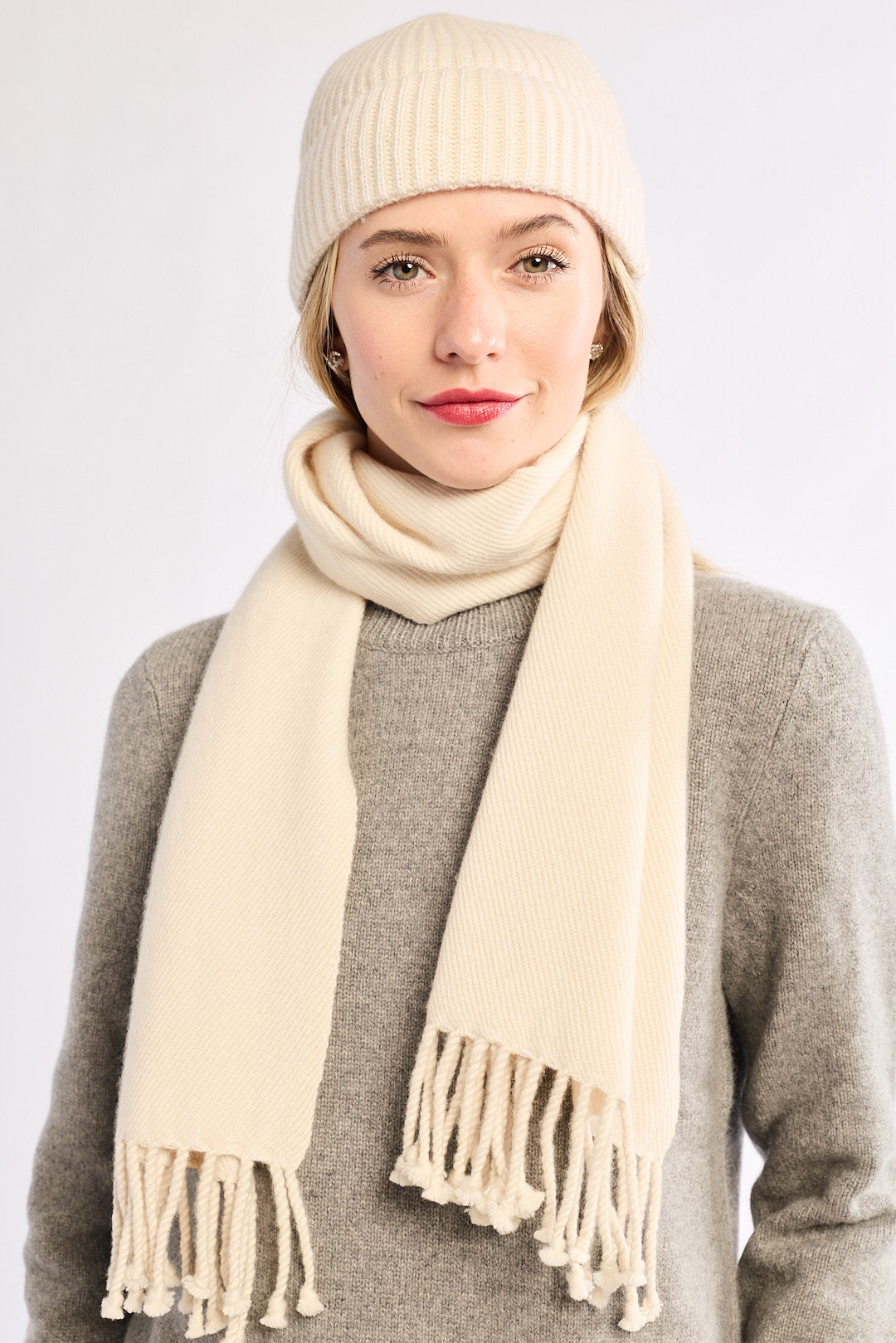 Woman wearing a cream beanie and scarf on a white background