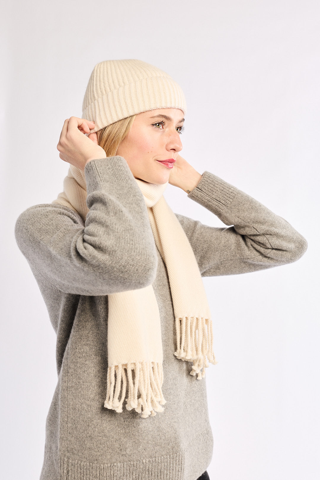 Woman wearing a beige knit hat and scarf with a gray sweater on a white background