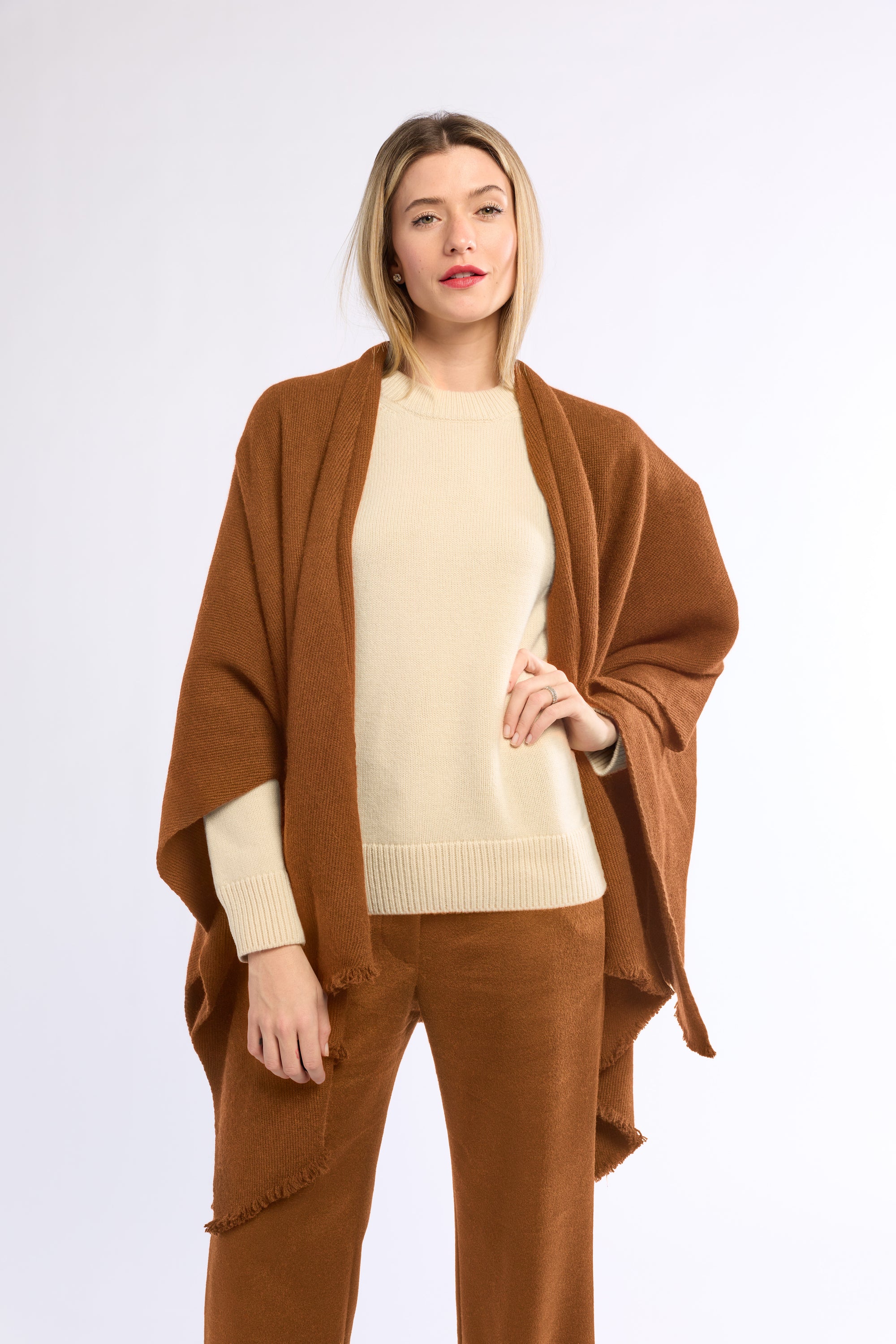 Woman wearing a brown poncho over a beige sweater and pants on a white background