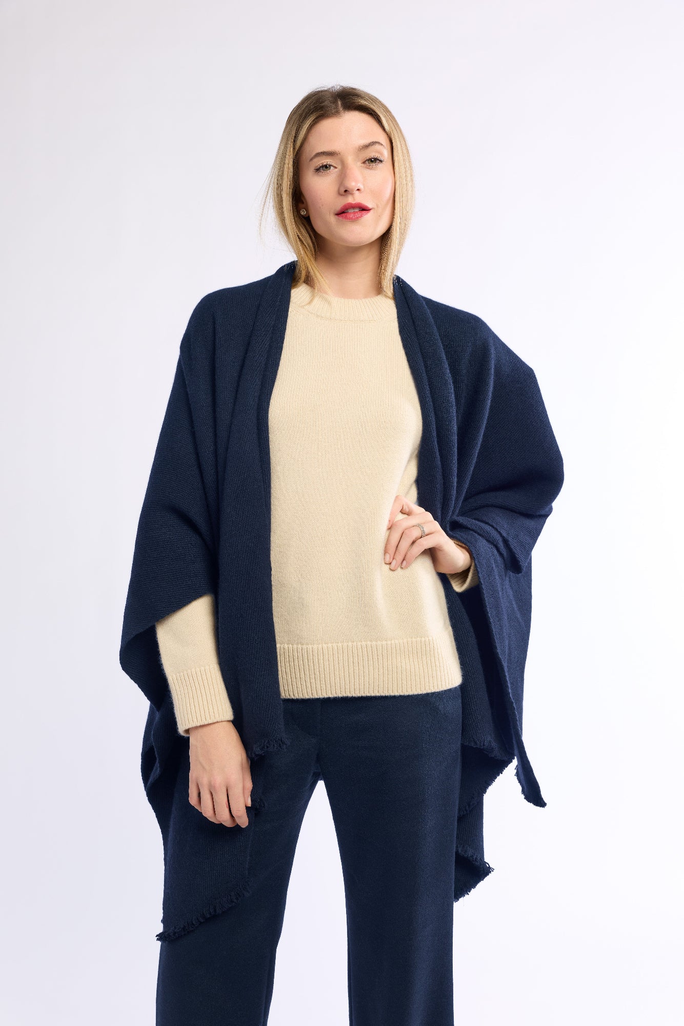 Woman wearing a navy blue poncho over a beige sweater and pants on a white background