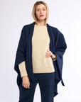 Woman wearing a navy blue poncho over a beige sweater and pants on a white background