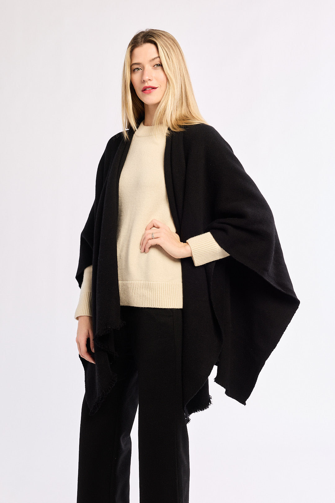Woman wearing a black poncho over a beige sweater on a white background