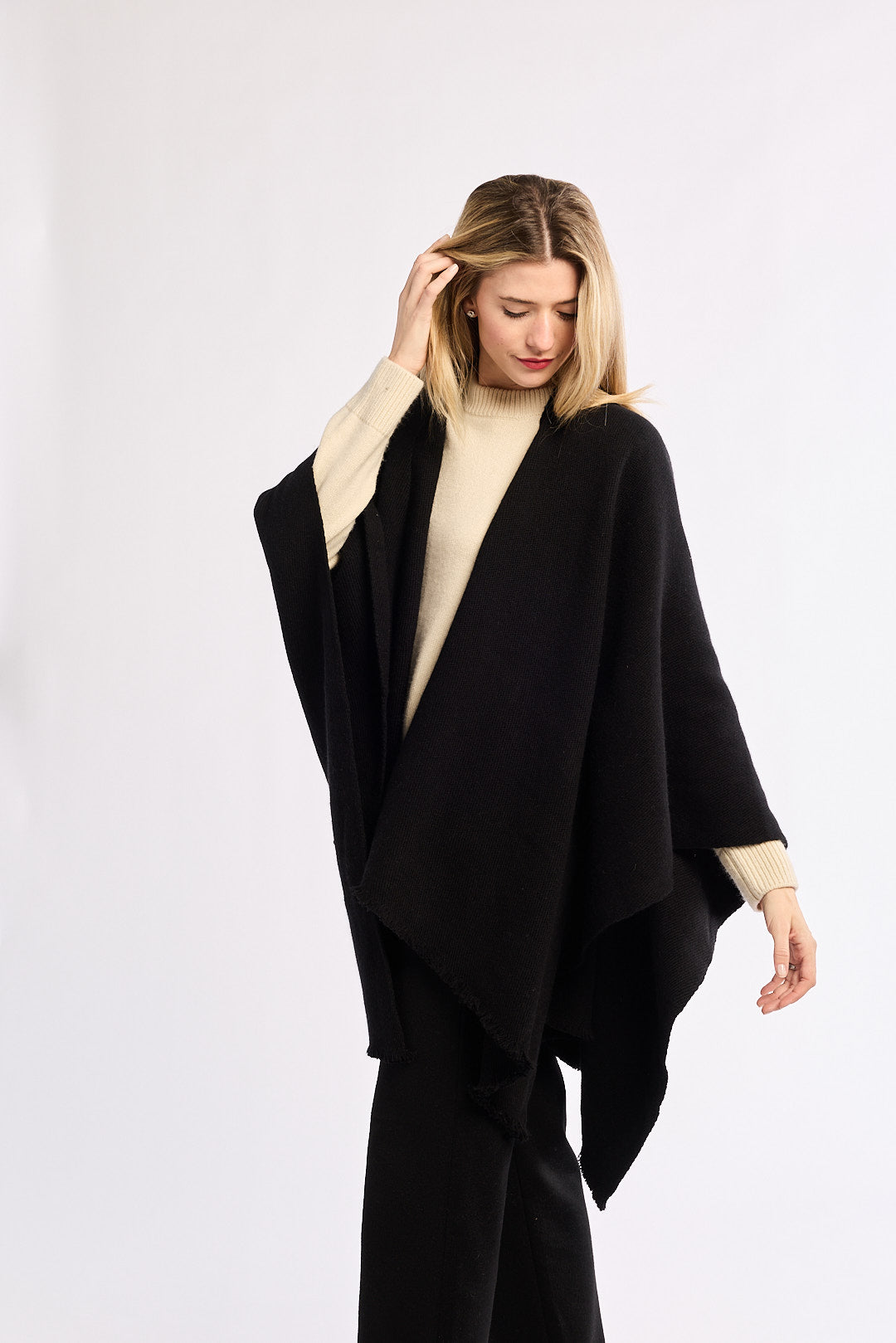 Woman wearing a black poncho over a beige top on a white background