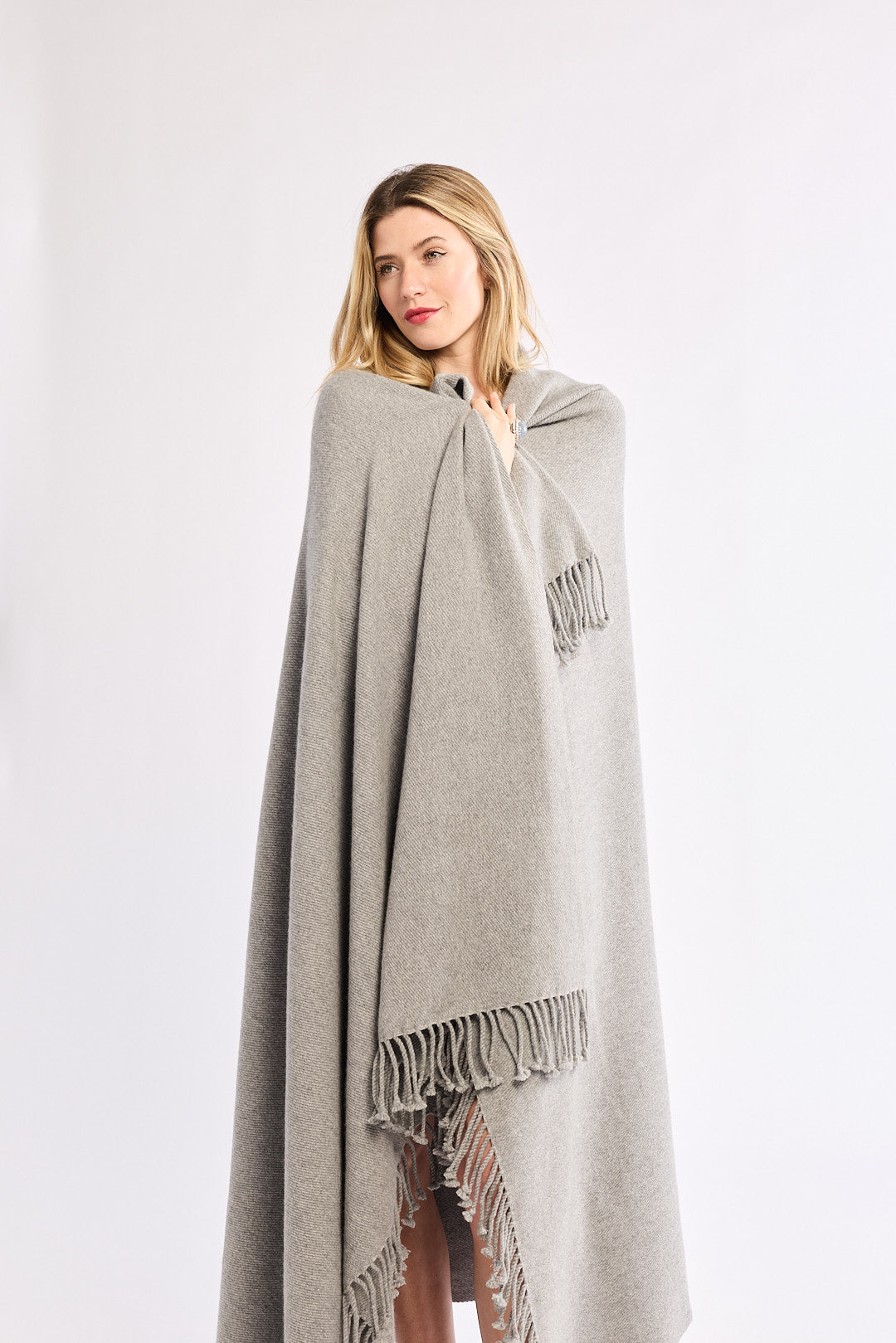 Woman wearing a gray blanket with fringe details on a white background
