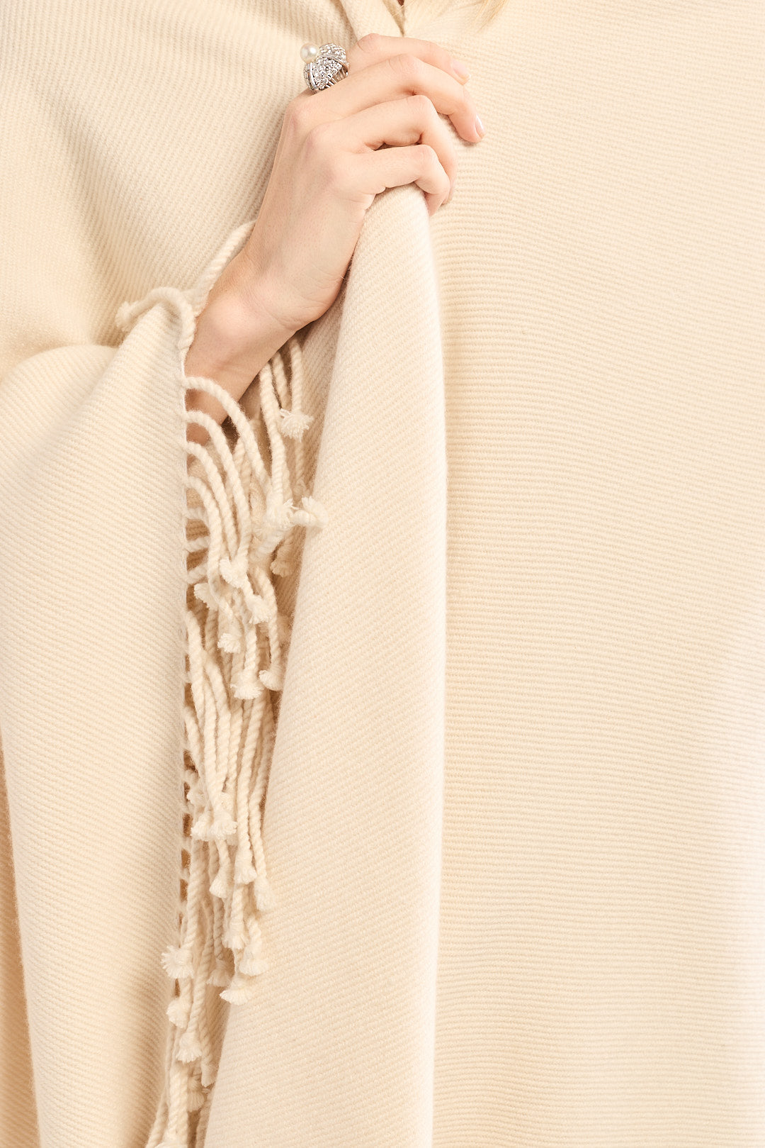 Beige scarf with fringe held by a hand against a beige background