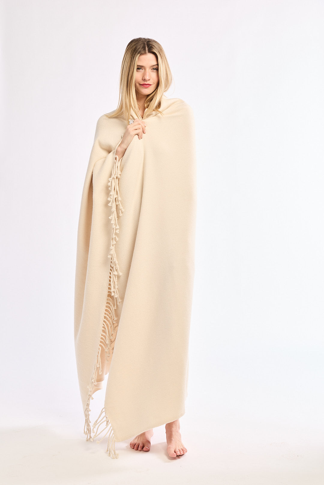 Woman wearing a beige poncho with fringe details on a white background