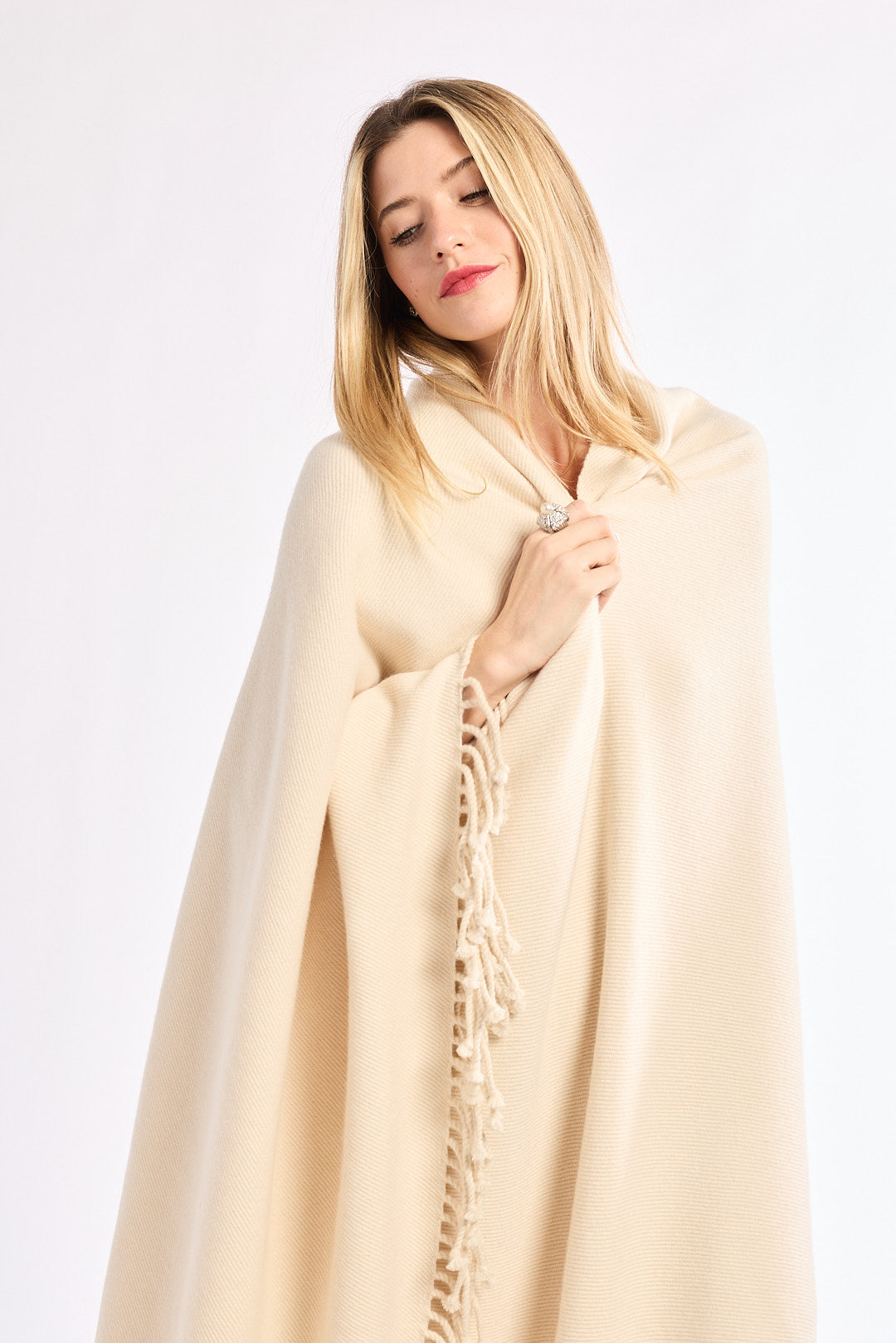 Woman wearing a beige blanket with tassels on a white background