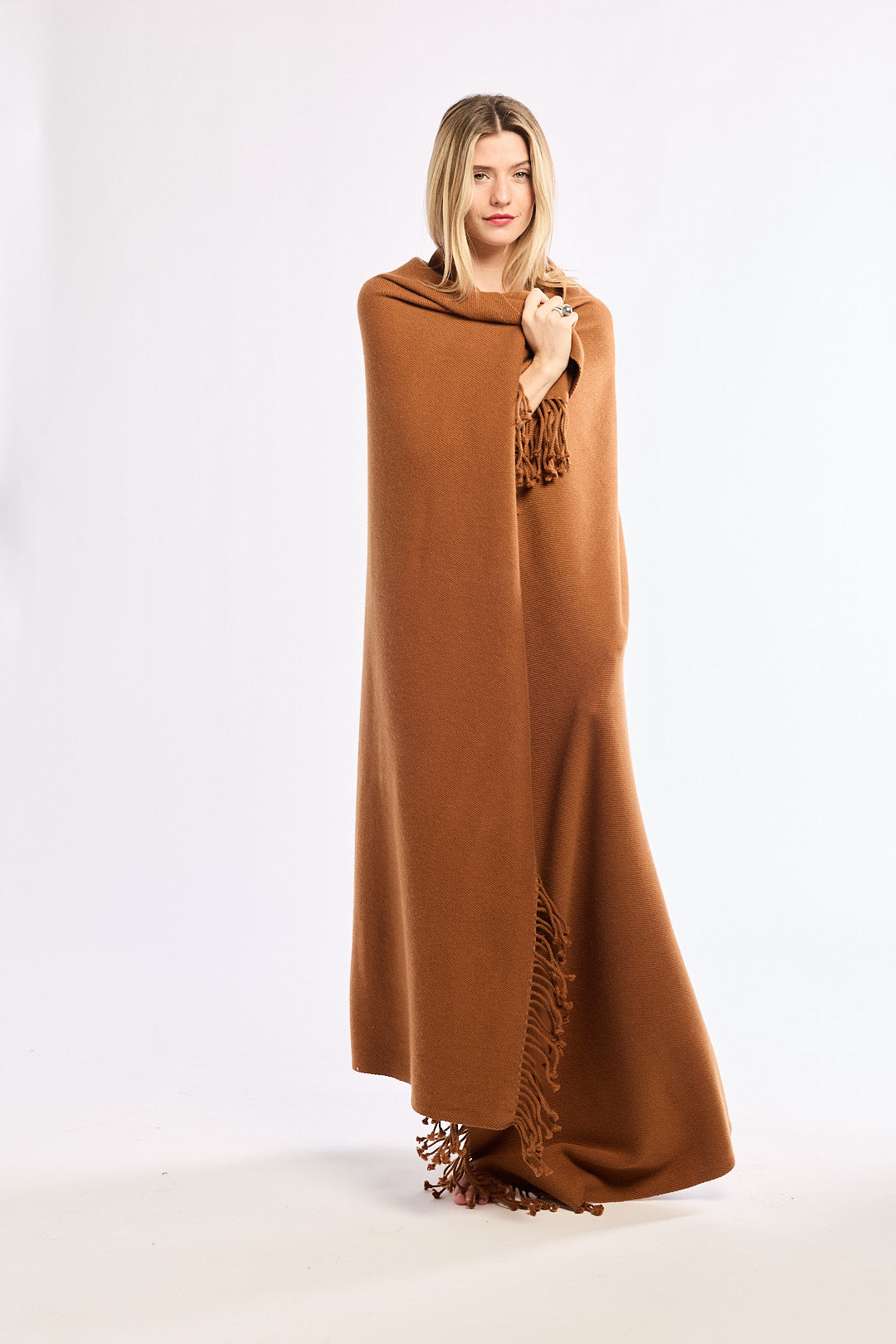 Woman wearing a long brown shawl with fringe details on a white background