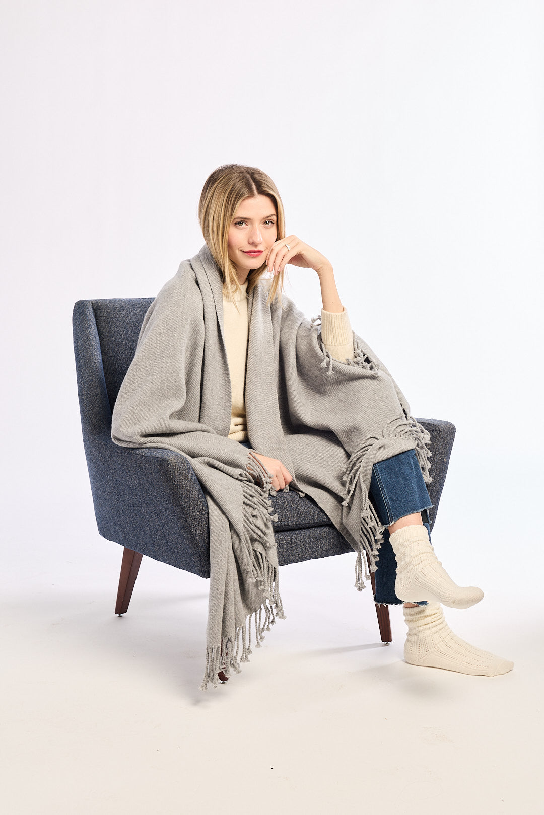 Woman sitting in a chair wearing a gray blanket draped over her shoulders on a white background