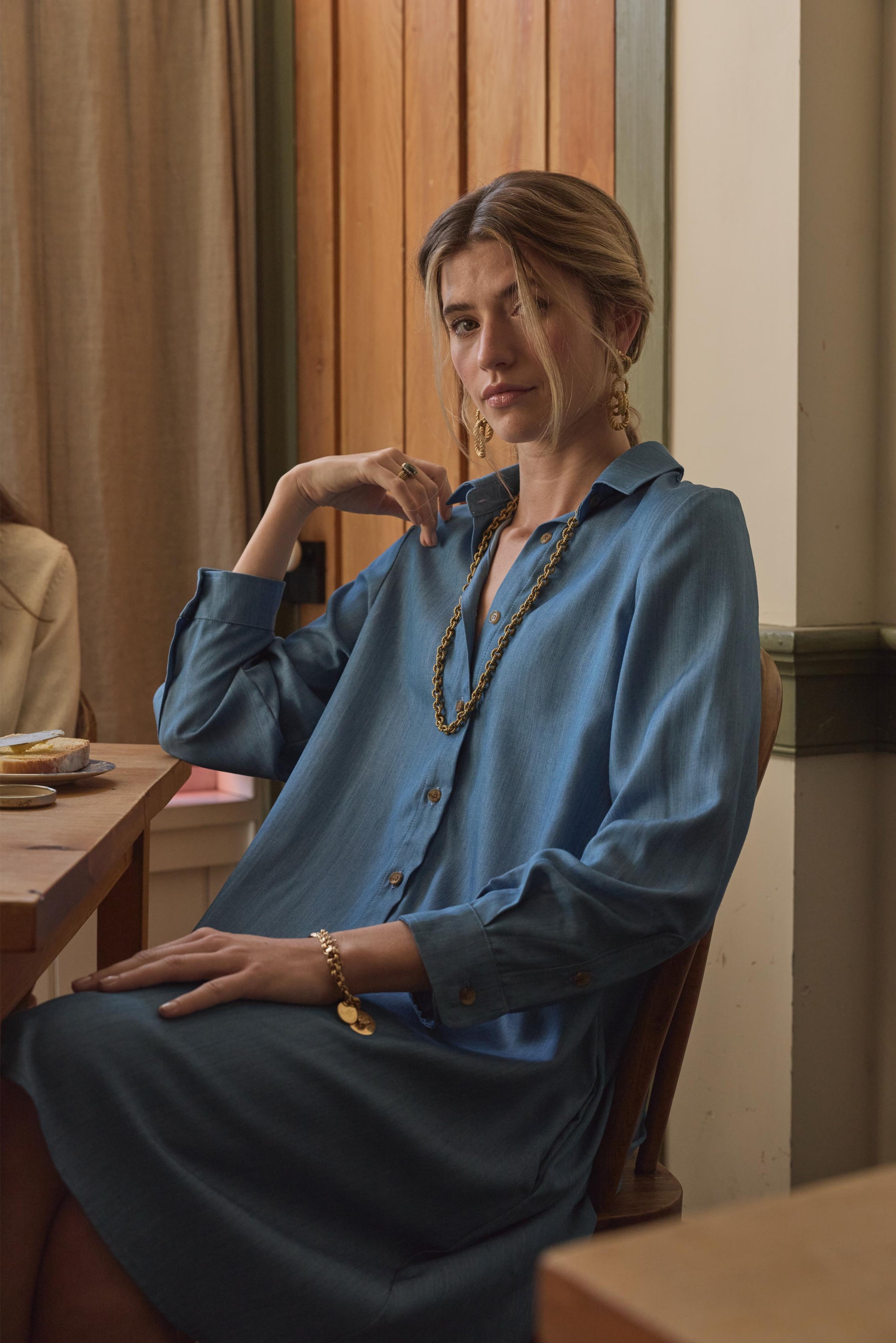 Woman sitting wearing blue dress and gold jewelry