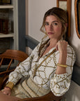 Woman sitting on a wooden chair wearing a patterned blouse in an indoor setting.