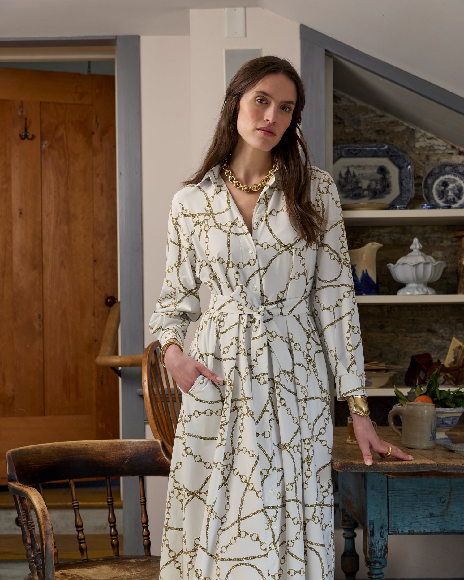 Woman modeling a white long sleeve dress with gold pattern in a house