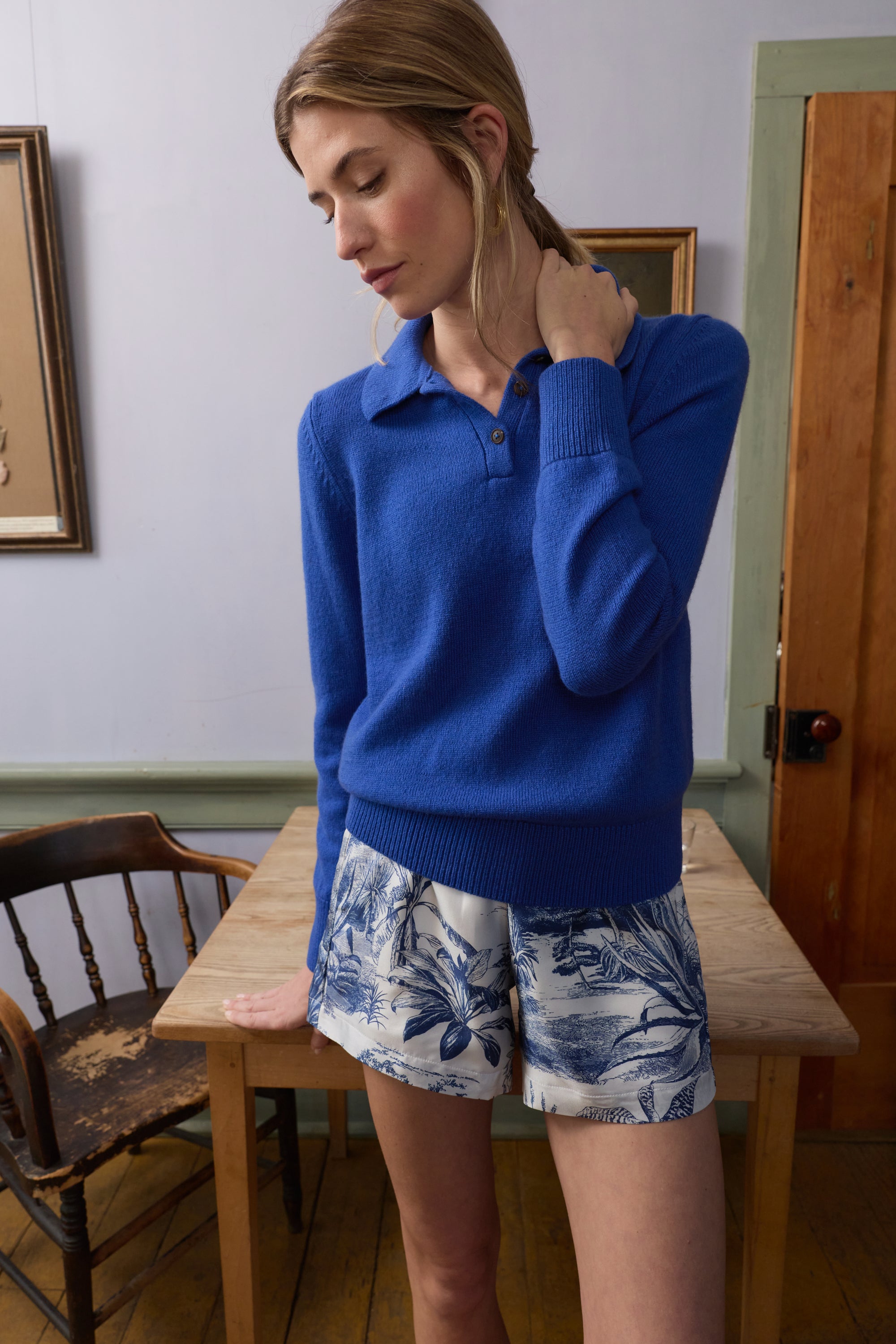 Woman wearing a blue sweater and floral shorts in a room with wooden furniture.