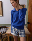 Woman wearing a blue sweater and floral shorts in a room with wooden furniture.