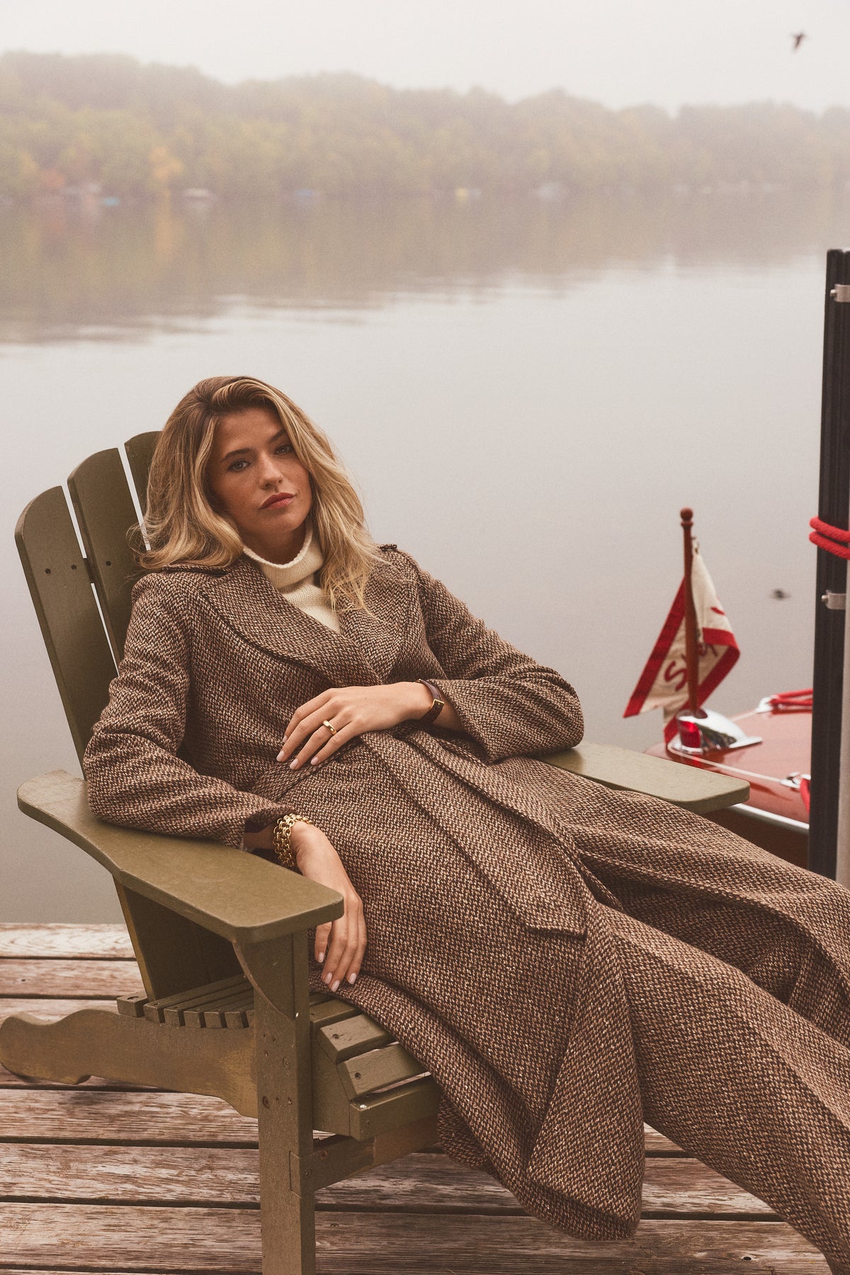 Woman modeling a long tweed coat in a chair outside