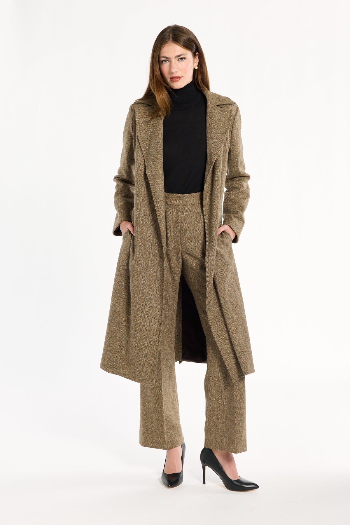 A woman modeling the Painter's Fleck Herringbone Anne Coat open over a black turtleneck and matching trousers, front view, photographed against a plain white studio background.