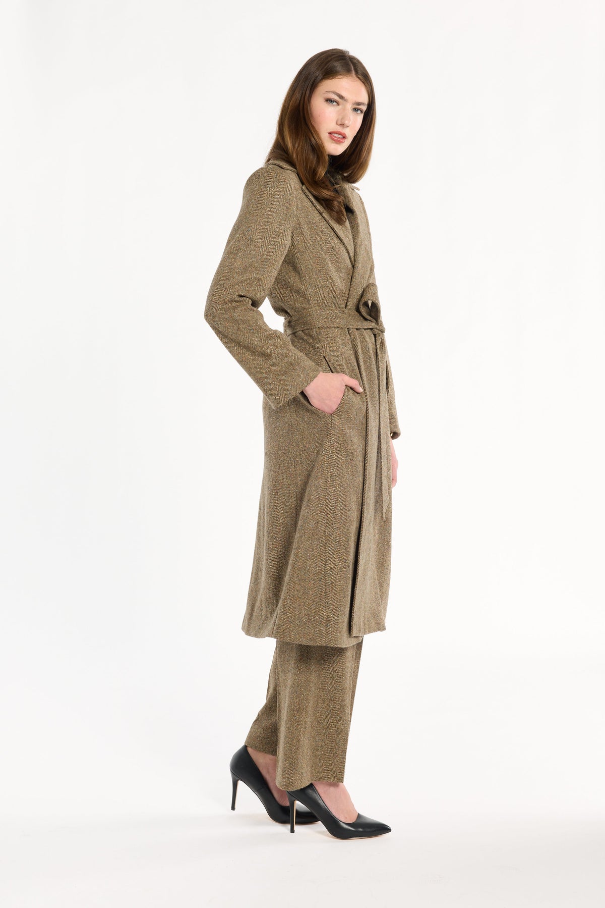 A woman modeling the belted Painter's Fleck Herringbone Anne Coat with matching trousers, three-quarter side view, photographed against a plain white studio background.