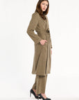 A woman modeling the belted Painter's Fleck Herringbone Anne Coat with matching trousers, three-quarter side view, photographed against a plain white studio background.