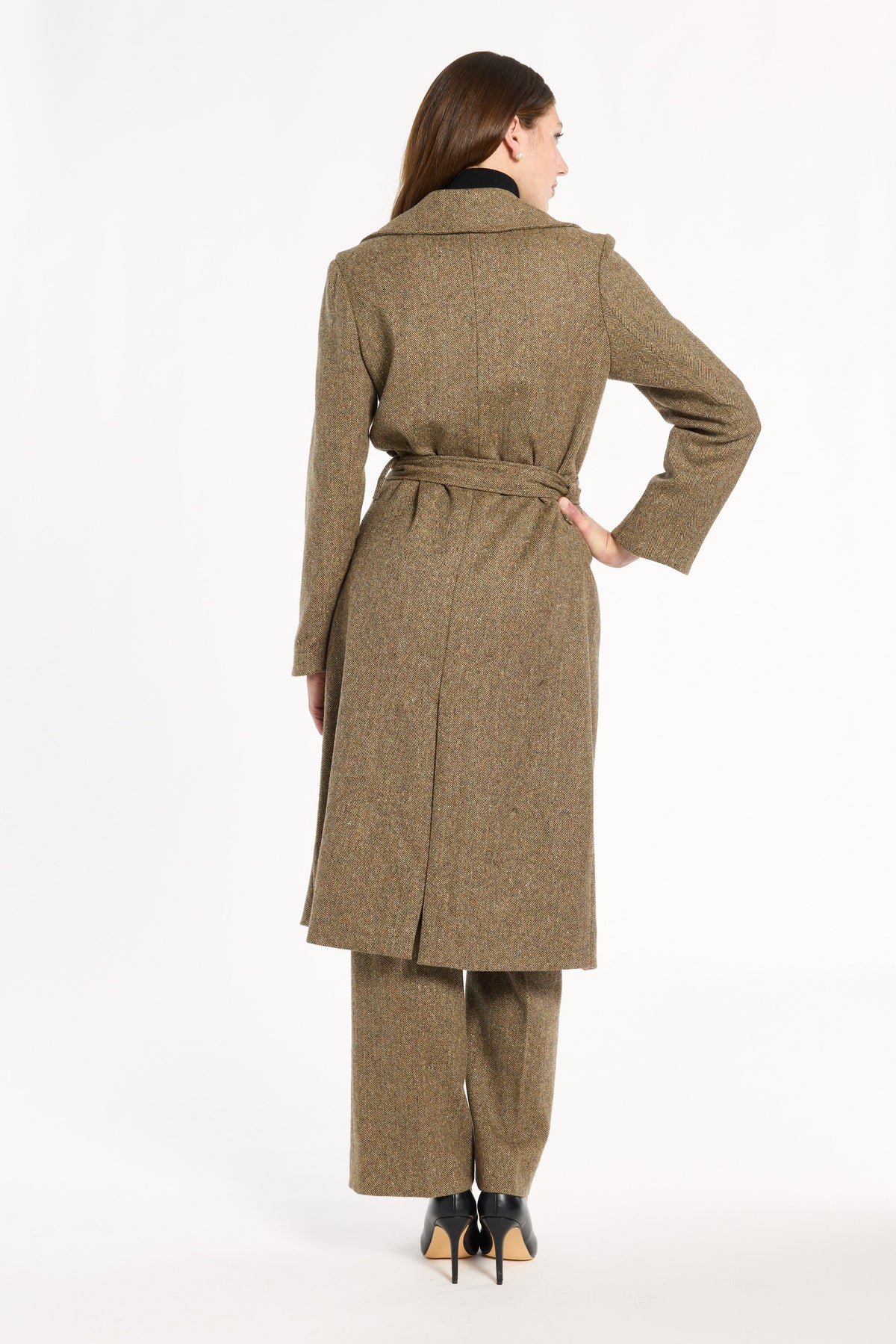 A woman modeling the belted Painter's Fleck Herringbone Anne Coat with matching trousers, back view, photographed against a plain white studio background.