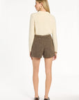 A woman modeling the Tobacco Tweed Archer Shorts with a cream sweater and brown loafers, back view, photographed against a plain white studio background.