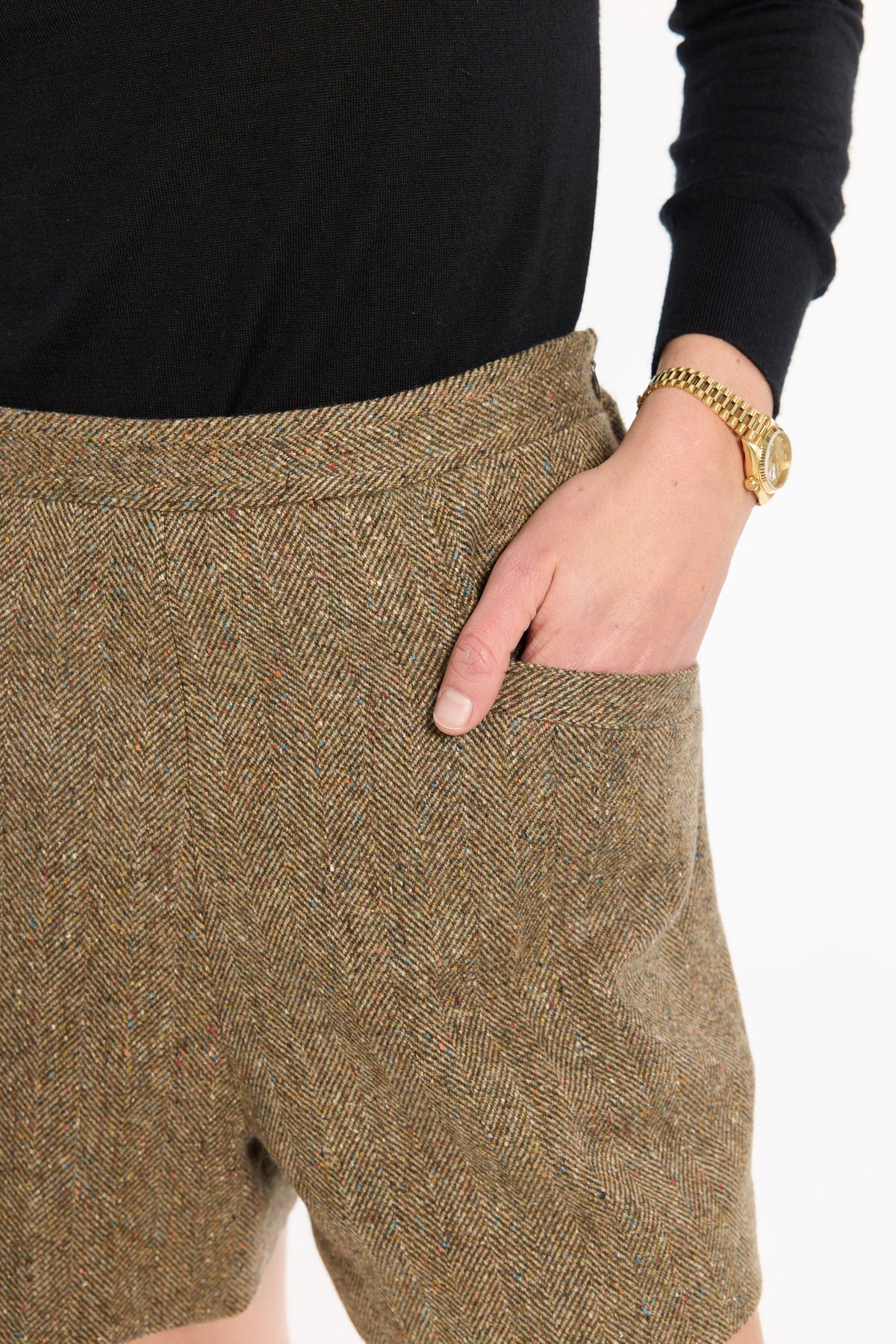 Close-up of a hand in the pocket of the Painter's Fleck Herringbone Archer Shorts, showing the waistband and tweed texture, photographed against a plain white studio background.