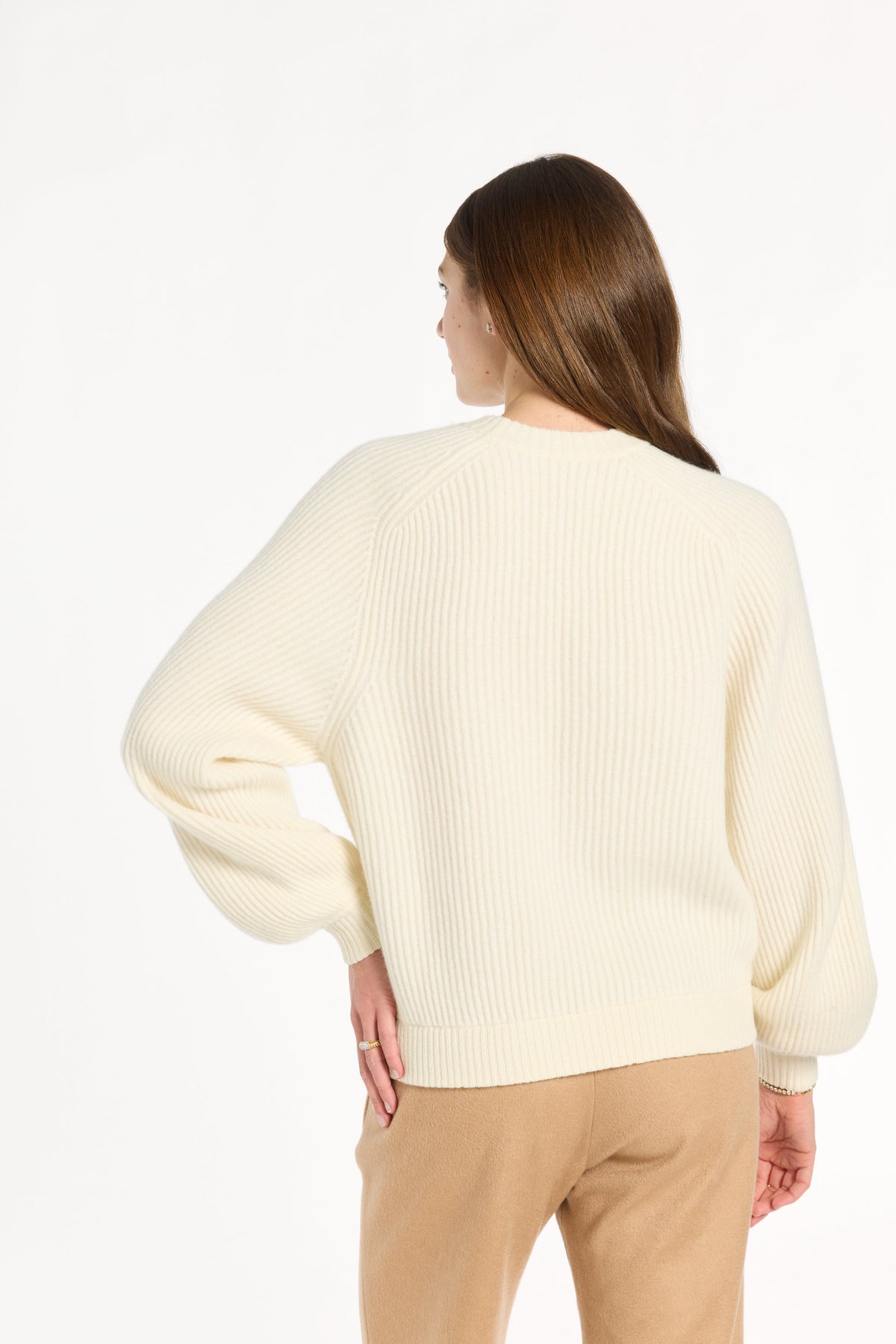 A woman modeling the cream Baby Cashmere Ribbed Crewneck with camel trousers, back view, photographed against a plain white studio background.