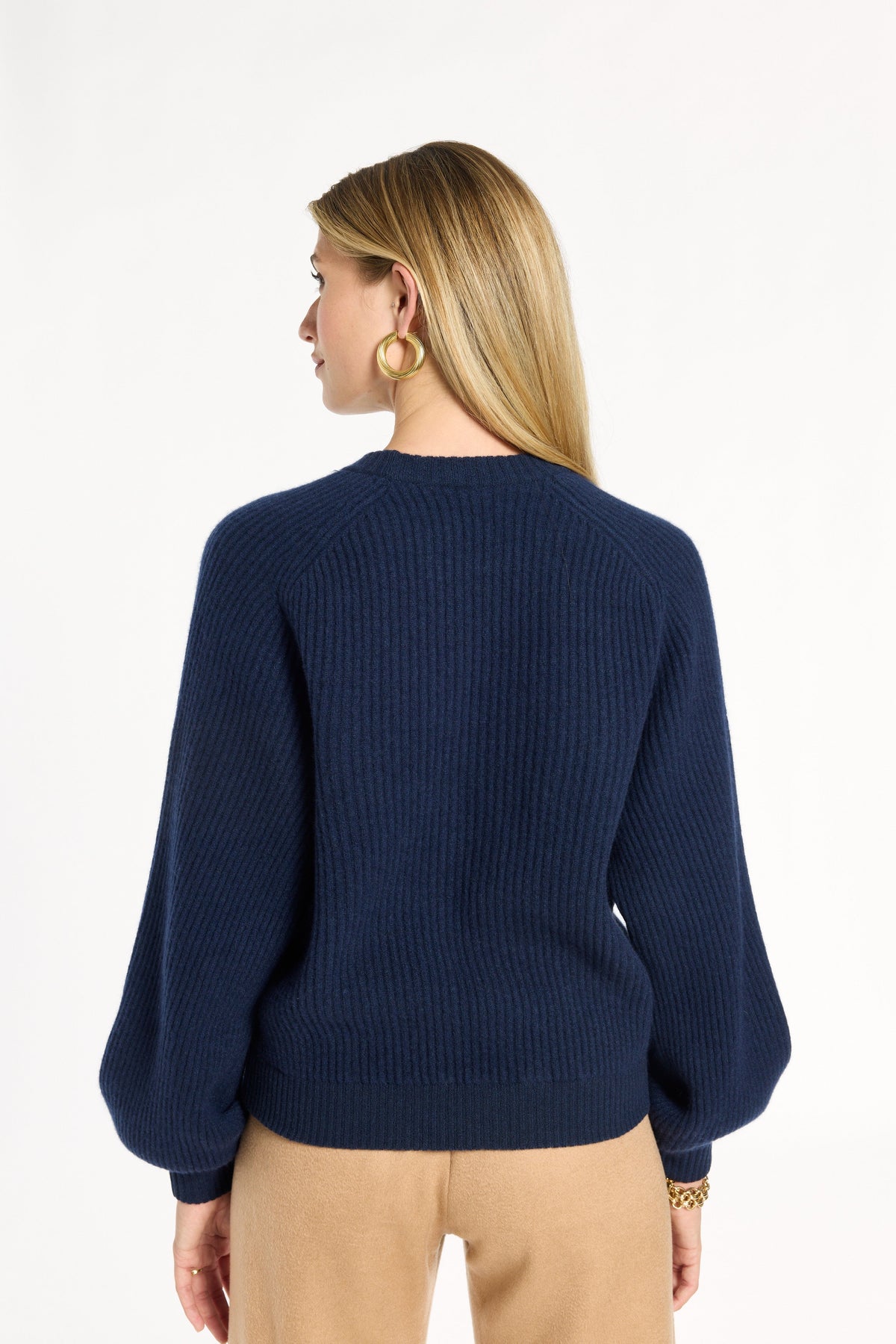 A woman modeling the navy Baby Cashmere Ribbed Crewneck with camel trousers, back view, photographed against a plain white studio background.