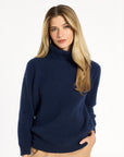 A woman modeling the navy Baby Cashmere Ribbed Turtleneck with camel trousers, front view, photographed against a plain white studio background.