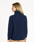 A woman modeling the navy Baby Cashmere Ribbed Turtleneck with camel trousers, back view, photographed against a plain white studio background.