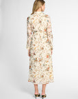 A woman viewed from the back wearing a long-sleeve midi dress with a cream base and an all-over multicolor floral print, paired with black pointed-toe heels against a light gray studio background.