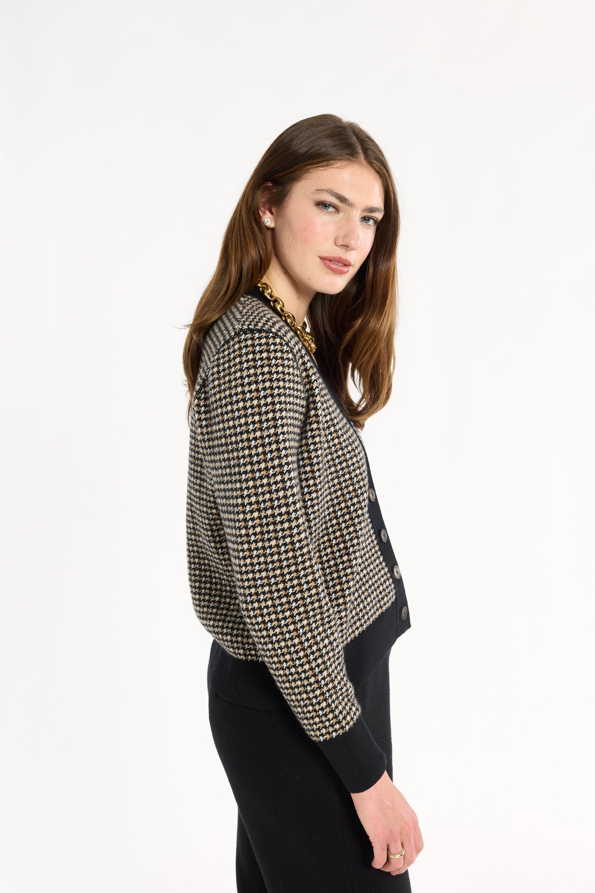 A woman modeling the Black Tri-Color Check Classic Cashmere Cardigan with black trousers, side view, photographed against a plain white studio background.
