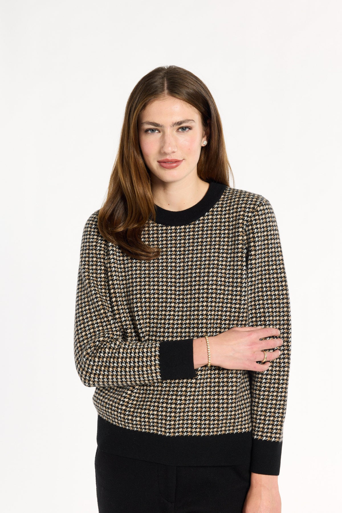 A woman modeling the Black Tri-Color Check Classic Cashmere Crew with black trousers, front view with arms crossed, photographed against a plain white studio background.