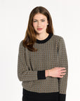 A woman modeling the Black Tri-Color Check Classic Cashmere Crew with black trousers, front view with arms crossed, photographed against a plain white studio background.