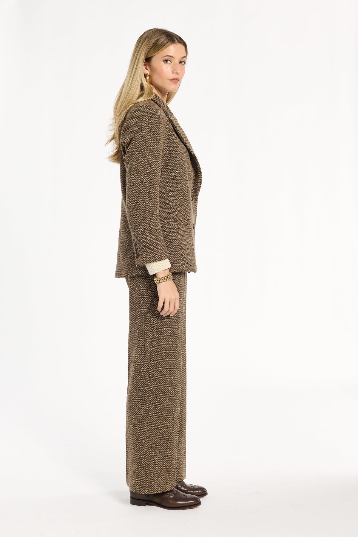 A woman modeling the Tobacco Tweed Cynthia Blazer with matching trousers, side view, photographed against a plain white studio background.