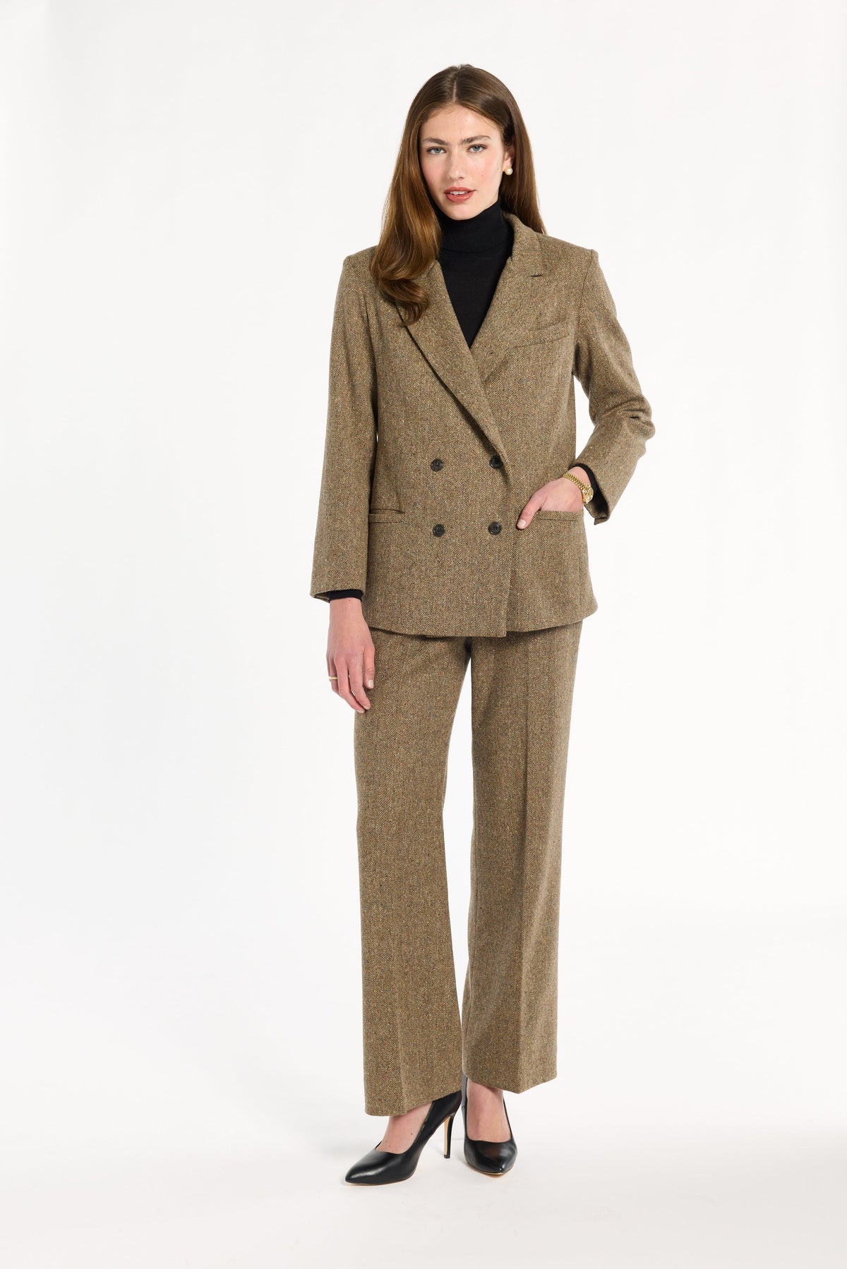 A woman modeling the double-breasted Painter's Fleck Herringbone Cynthia Blazer with a black turtleneck and matching trousers, front view, photographed against a plain white studio background.