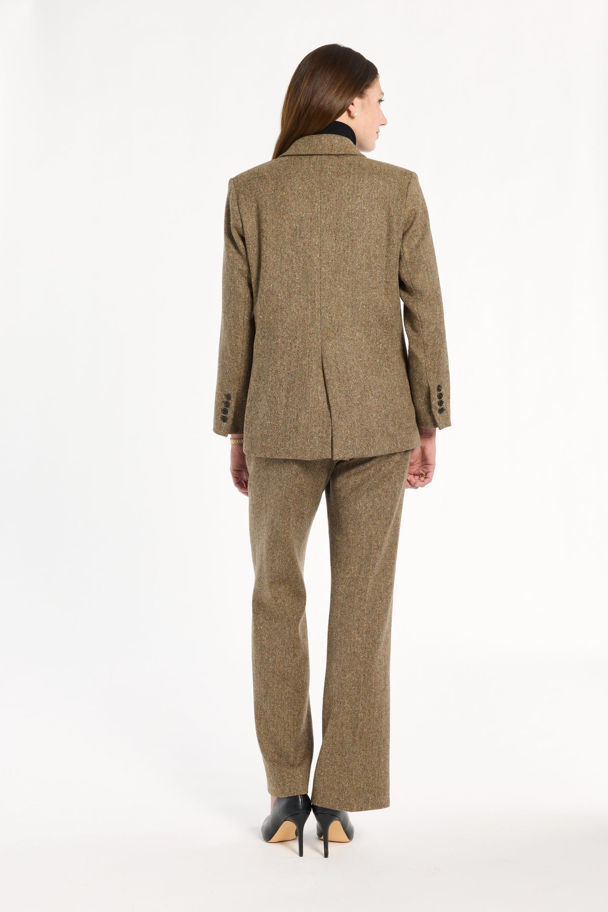 A woman modeling the Painter's Fleck Herringbone Cynthia Blazer with matching trousers, back view, photographed against a plain white studio background.