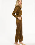 A woman modeling the Golden Umber Diane Pants with the coordinating Eleanor Shirt and cream heels, side view, photographed against a plain white studio background.