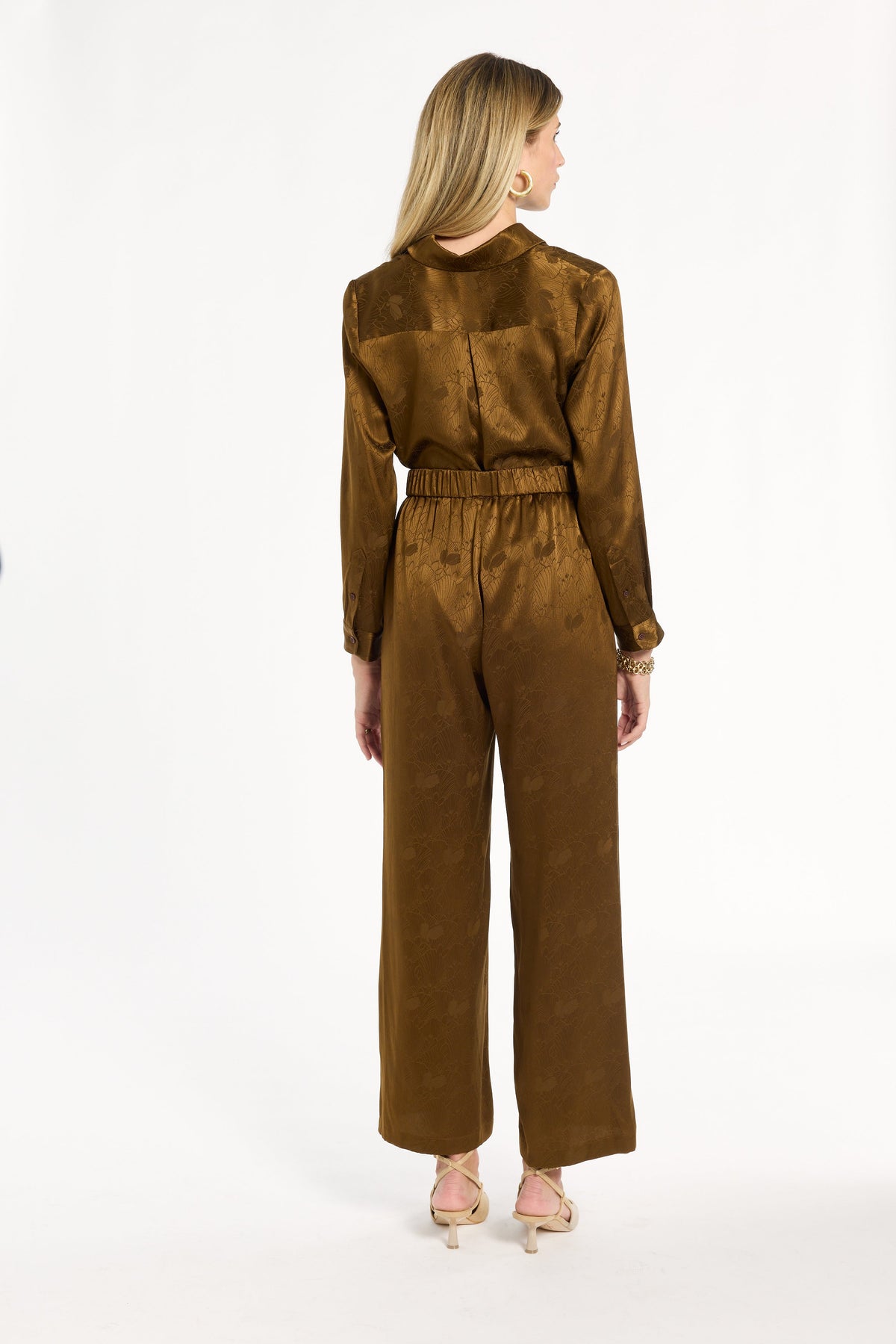 A woman modeling the Golden Umber Diane Pants with the coordinating Eleanor Shirt, back view, photographed against a plain white studio background.