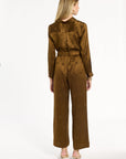 A woman modeling the Golden Umber Diane Pants with the coordinating Eleanor Shirt, back view, photographed against a plain white studio background.