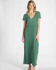A woman modeling a green short-sleeve dress with a V-neckline and subtle crinkle texture, standing against a gray background.