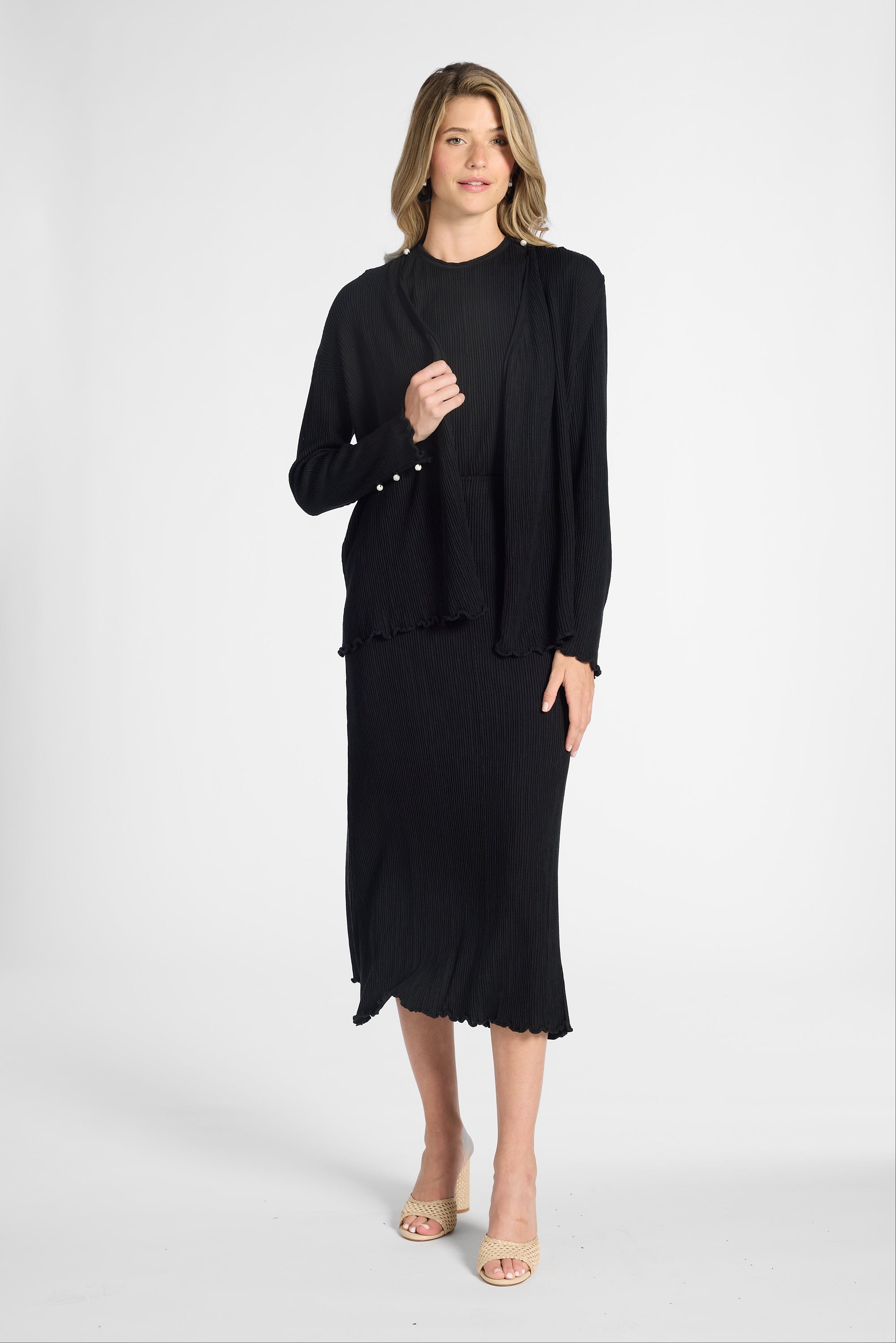 Woman wearing a black long sleeve cardigan over a black shell and skirt on a white backdrop