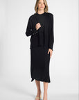Woman wearing a black long sleeve cardigan over a black shell and skirt on a white backdrop