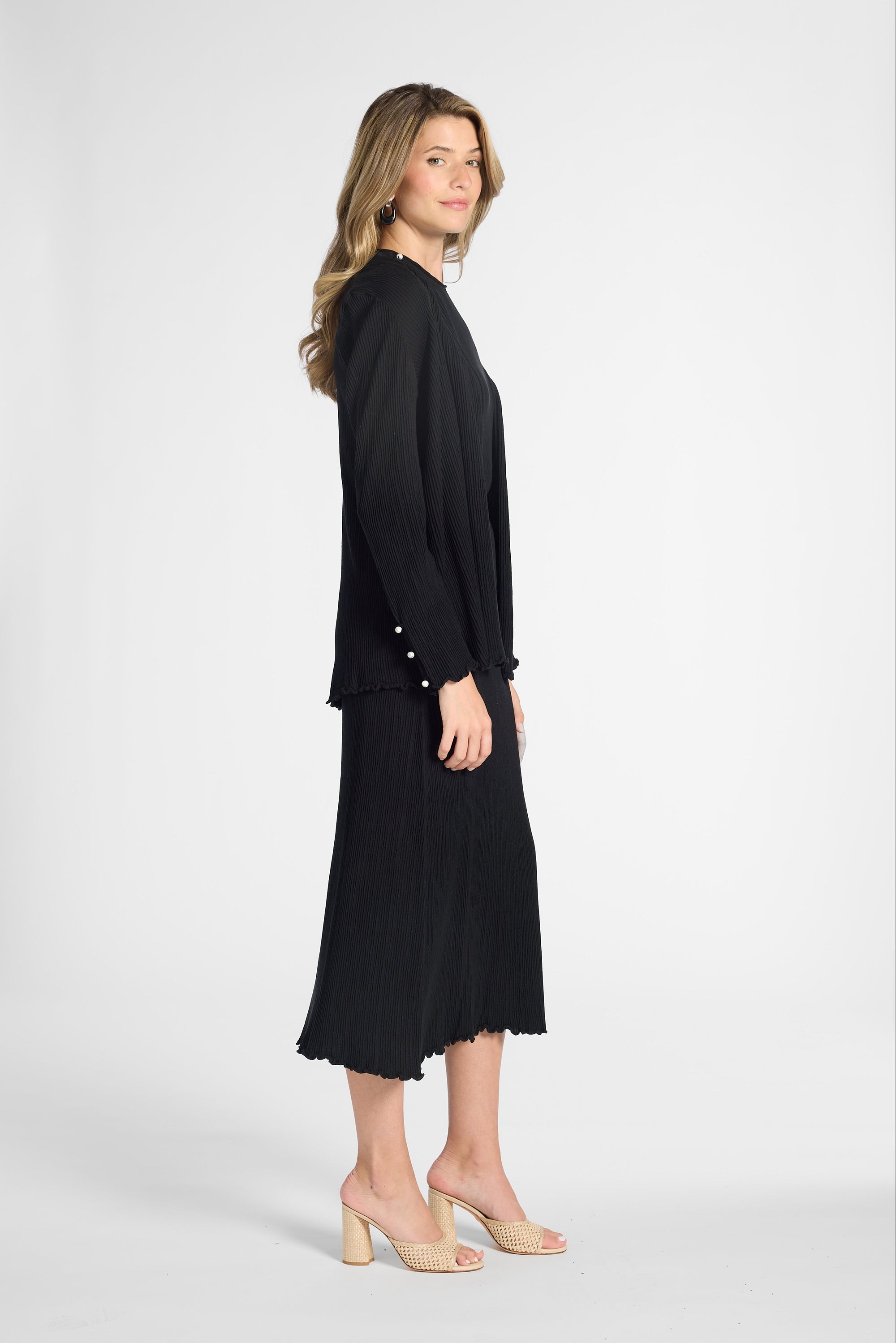 Woman modeling a long sleeve black cardigan over the matching black shell and skirt on a white backdrop