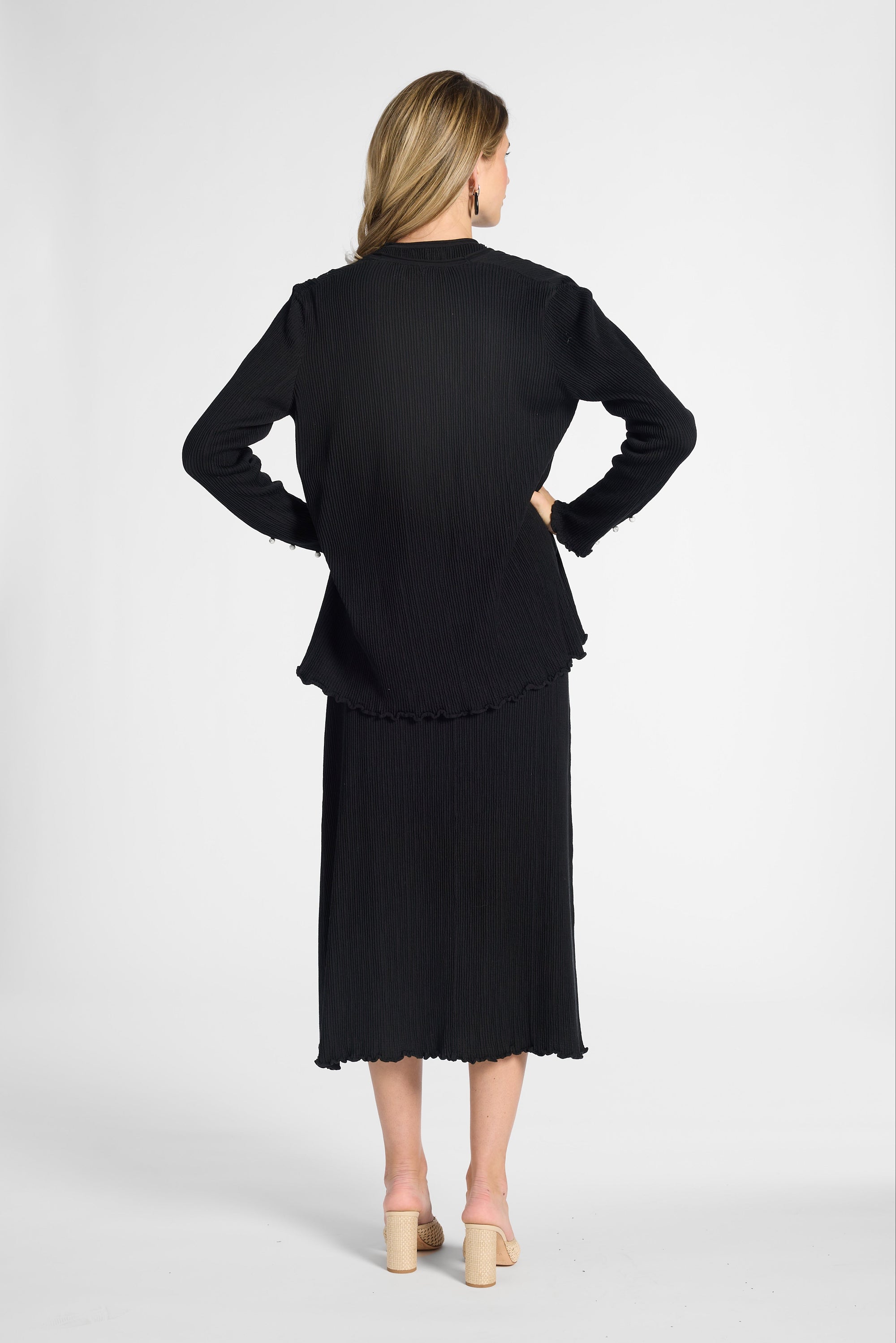 A woman shown from the back wearing a black long-sleeve cardigan and matching midi skirt set on a white backdrop