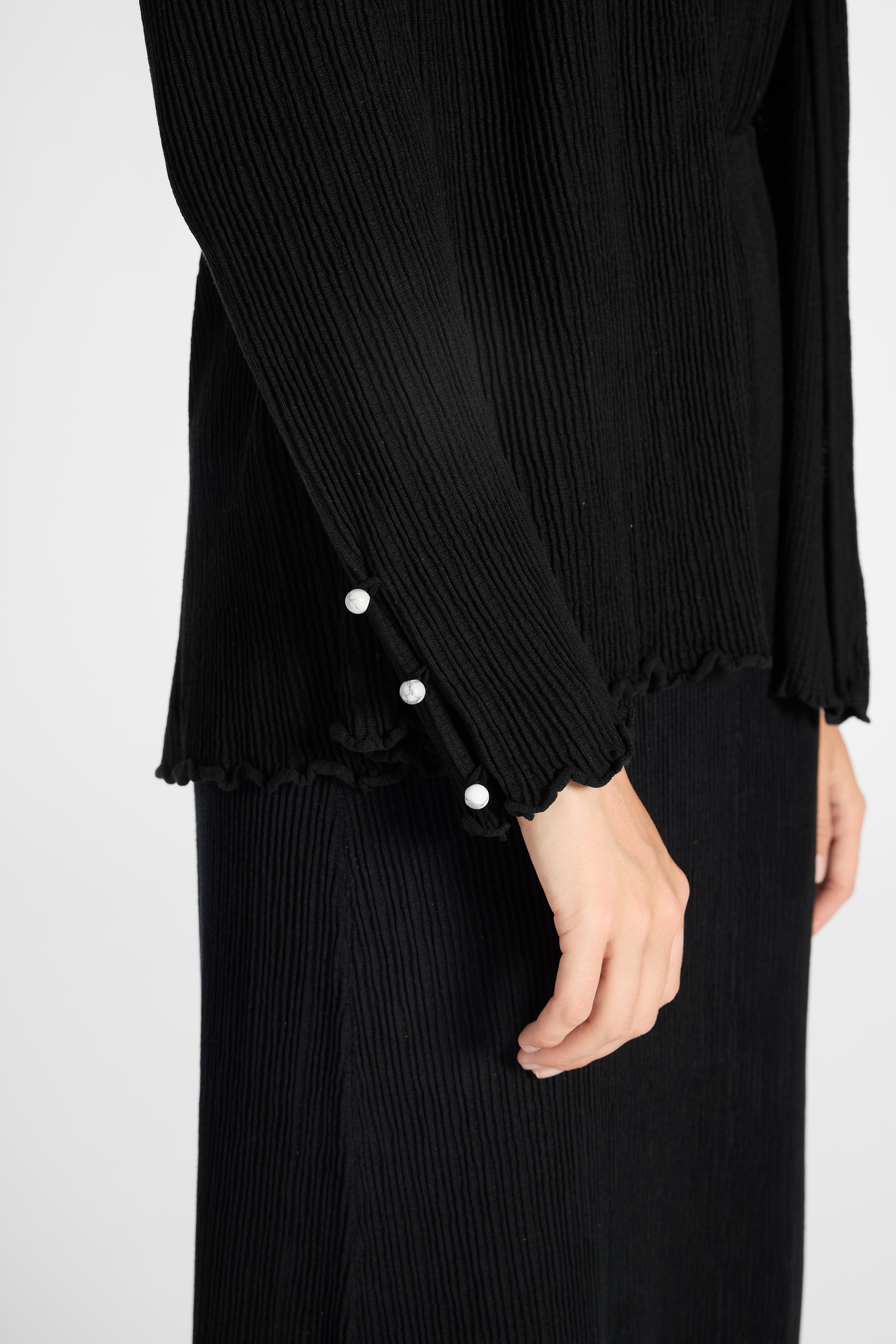 Close up of pleated black cardigan with gemstones buttons on the sleeve on a white backdrop
