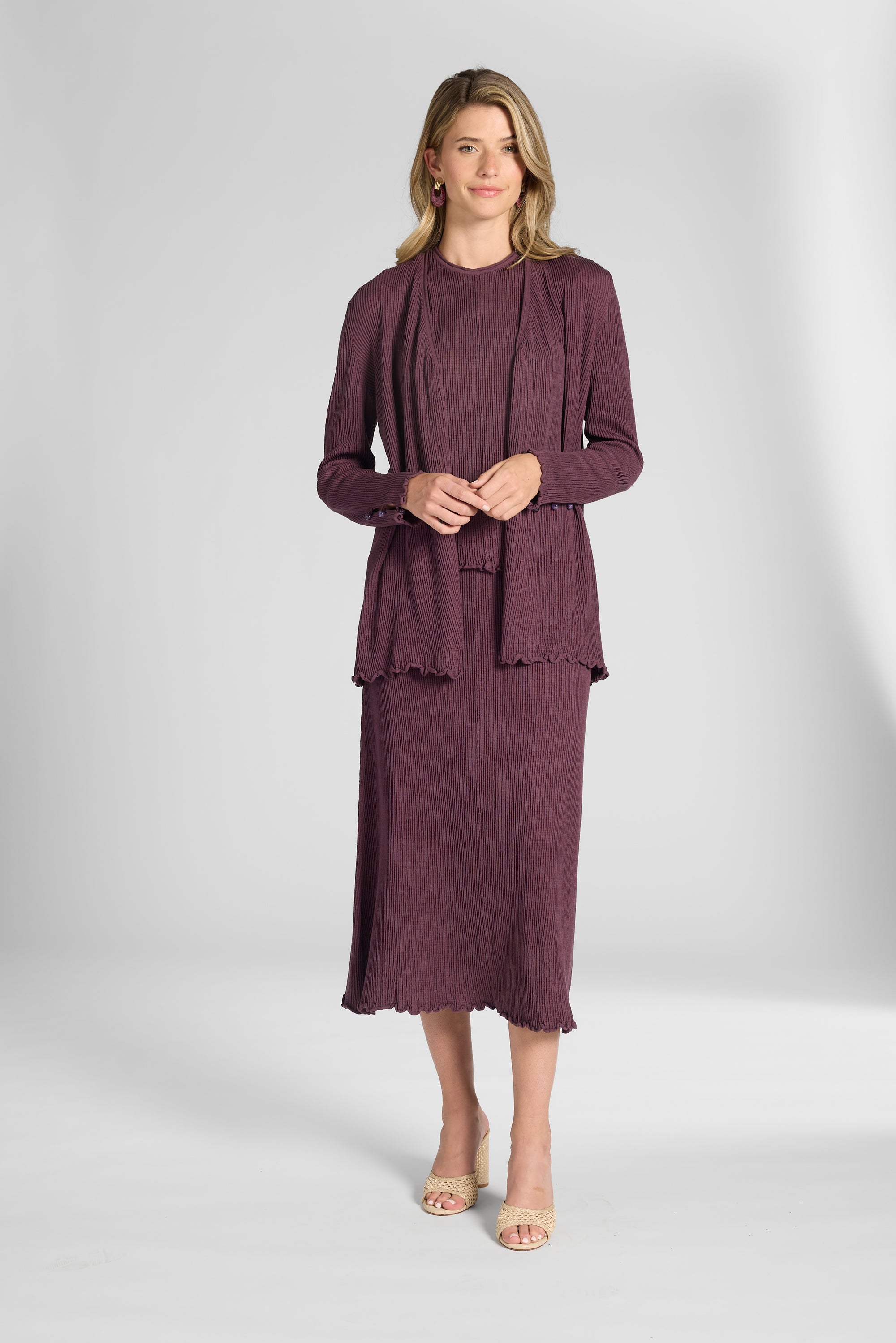 Woman modeling a pleated purple cardigan on a white backdrop