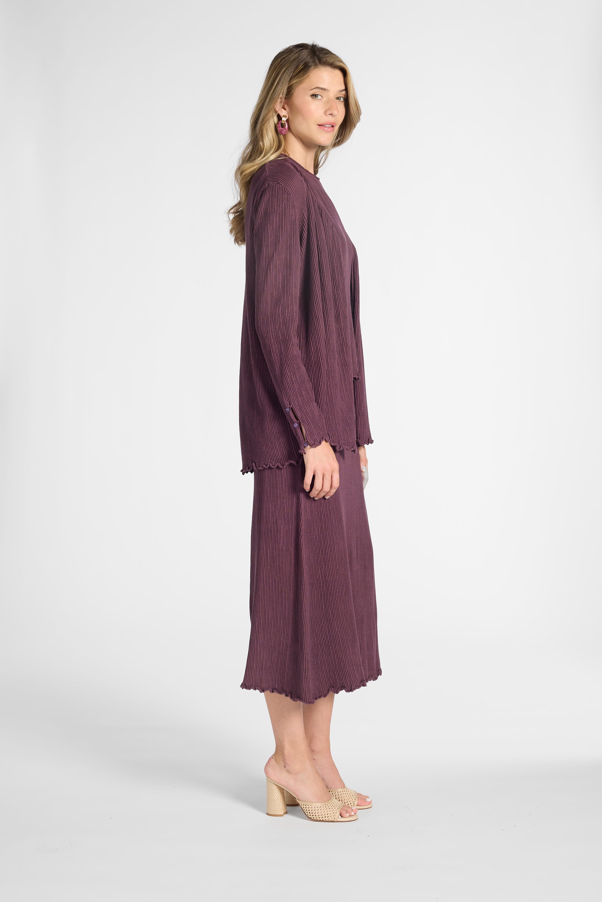 Woman wearing a pleated purple cardigan and skirt on a white backdrop
