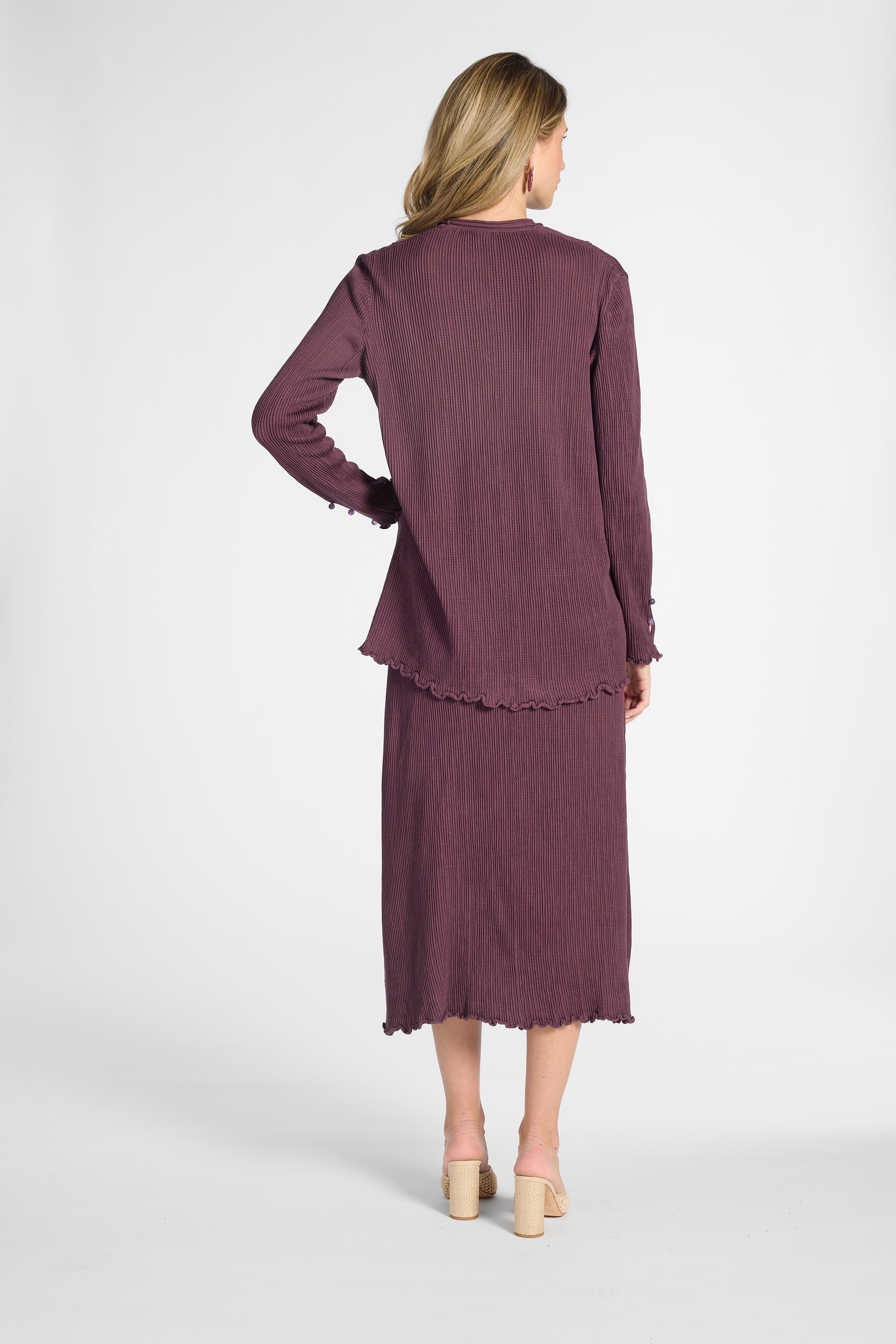 Woman modeling a silk pleated purple cardigan and the matching skirt on a white backdrop
